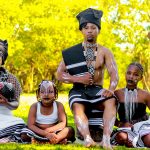 Grupo de pessoas usando trajes tradicionais Xhosa em um ambiente externo.