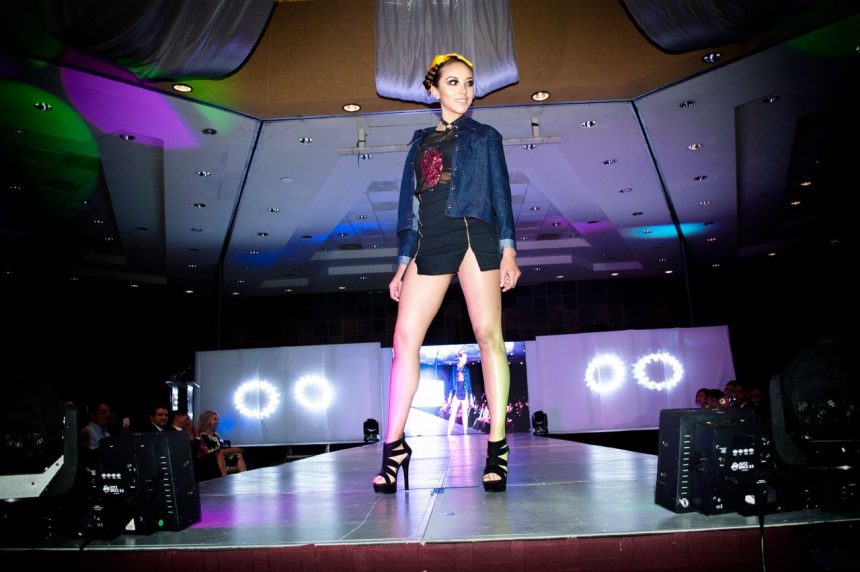 Modelo apresenta um look em uma passarela iluminada durante um desfile de moda.