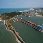 Vista aérea do porto de Imbituba, com docas, guindastes e a costa brasileira.