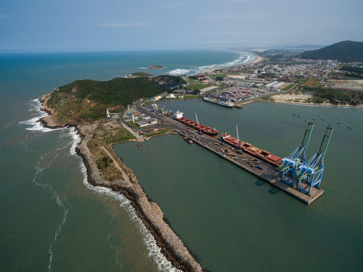 Vista aérea do porto de Imbituba, com docas, guindastes e a costa brasileira.