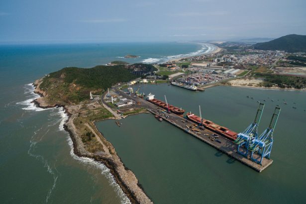 Vista aérea do porto de Imbituba, com docas, guindastes e a costa brasileira.