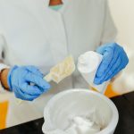 Técnico de laboratório usando luvas mistura uma formulação cremosa para pesquisa cosmética.