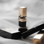 Produtos de beleza da YSL dispostos sobre um tecido claro, em composição de luxo.